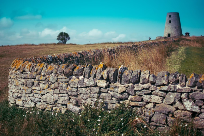 a stone wall with moss growing on top of it and a tower in the distance