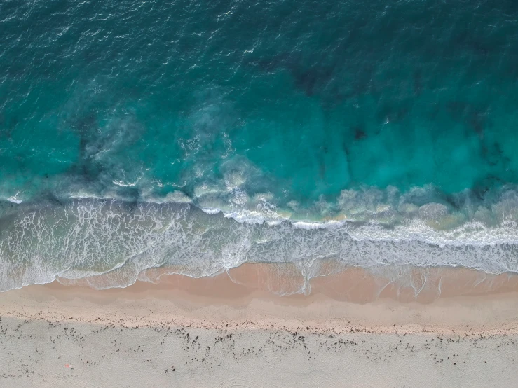 aerial view of sandy shoreline next to a clear blue ocean