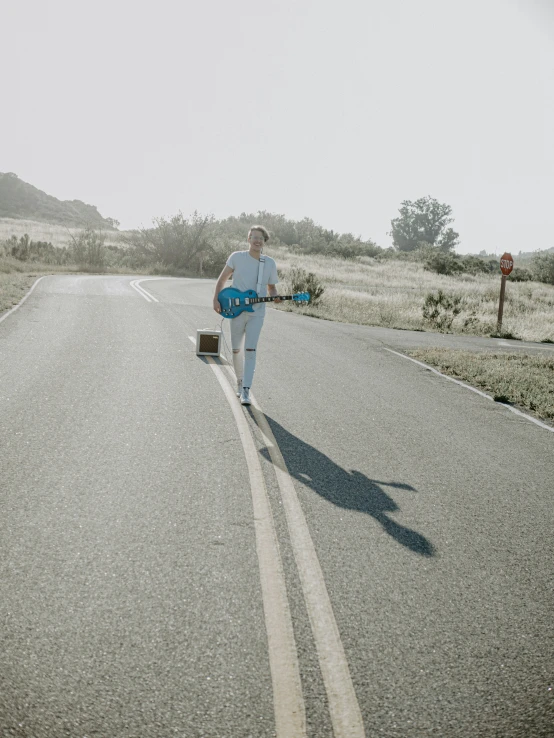 man walking down road carrying luggage and wearing white shirt