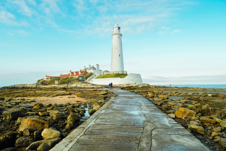 a walkway leads to a white lighthouse next to the ocean