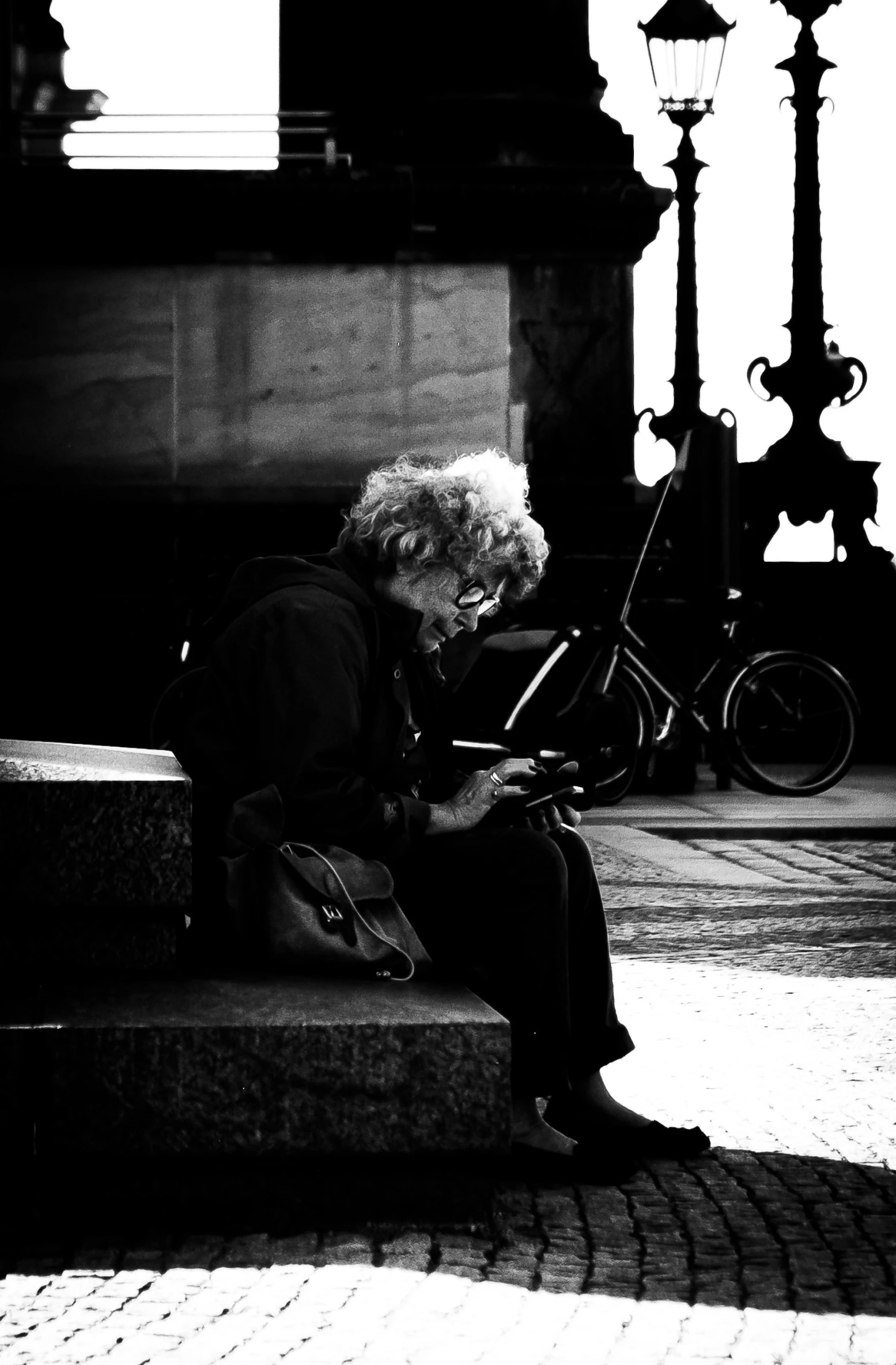 an older woman sitting outside on a bench, looking at her laptop