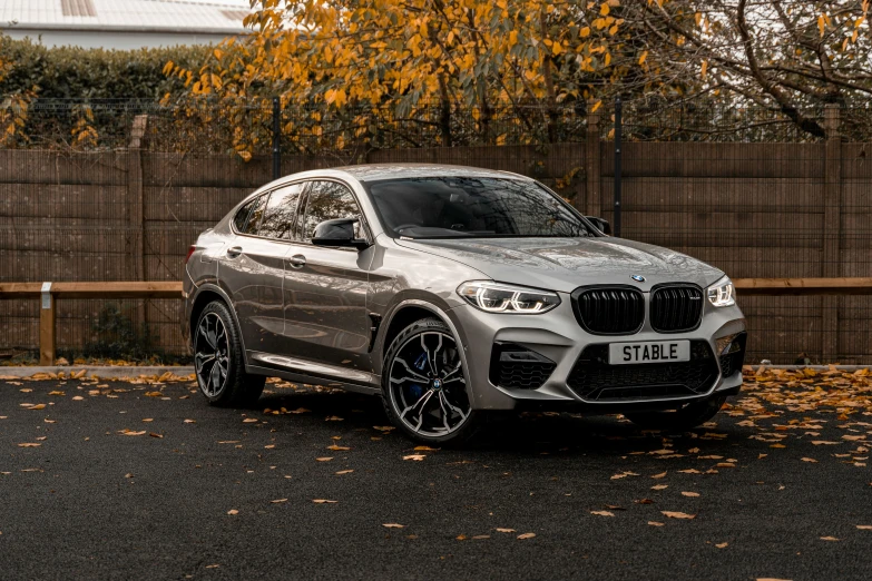 a silver bmw x4 parked in front of a wooden fence