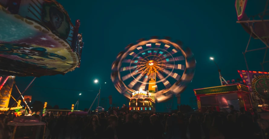 the view of an amut park at night, with ferris wheel in foreground