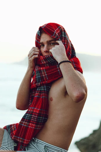 shirtless man covering himself with plaid on his head while sitting on beach