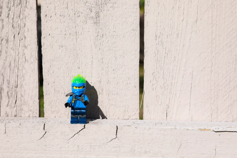 a toy figurine with a green helmet stands next to a fence