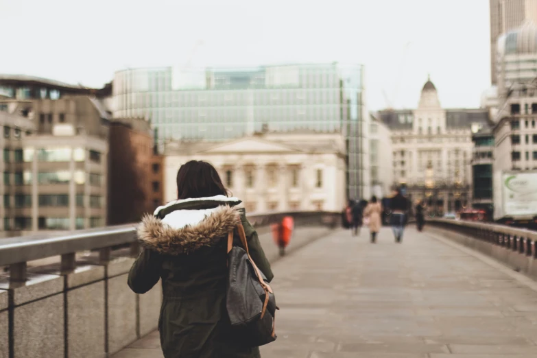 the woman is walking down the bridge wearing an oversize coat