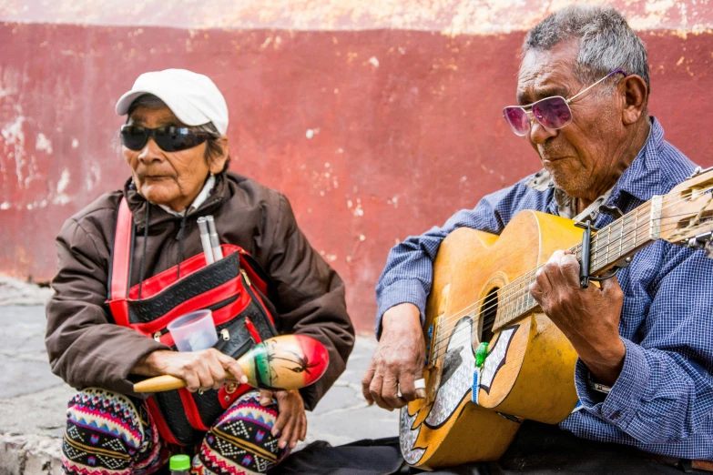 two old men sit together holding guitar and a wooden instrument