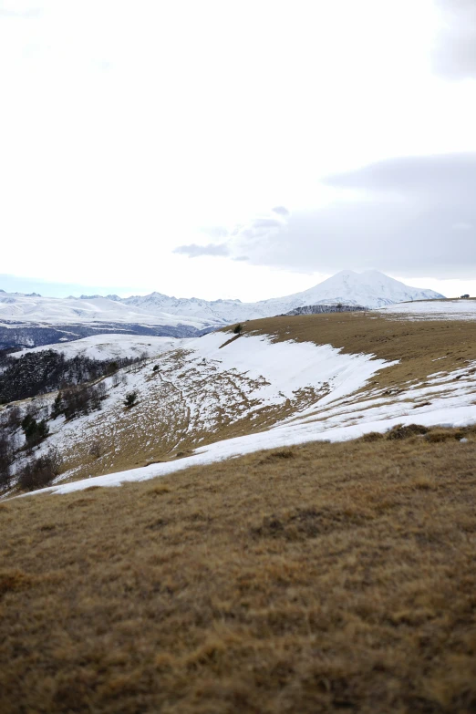 an open hill with snow on the ground and hills and a few trees