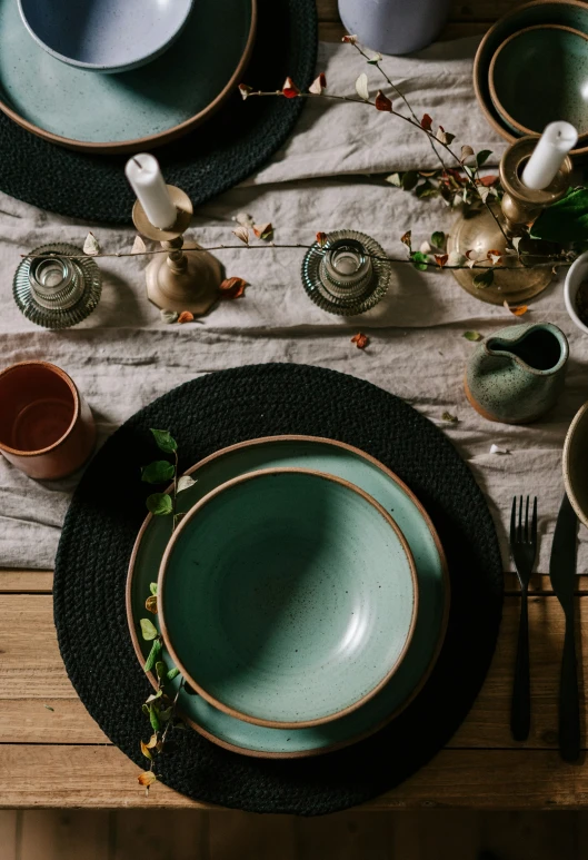 a place setting with dark green plates, green bowls and silverware