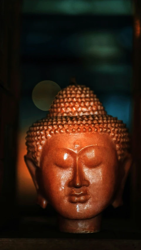an orange buddha head in a wooden shelf