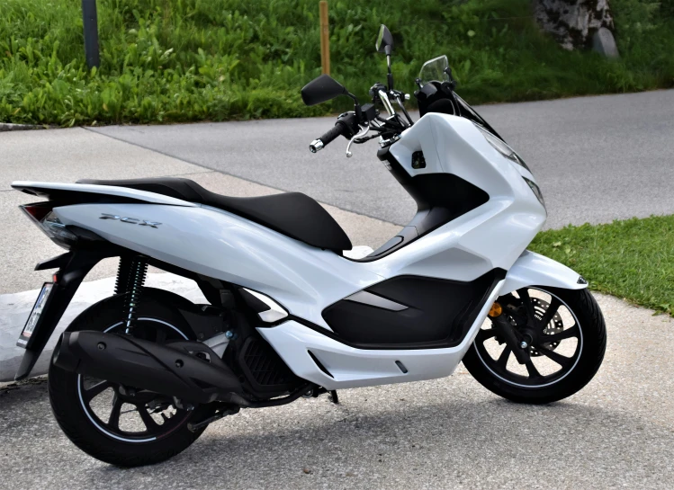 a scooter sits parked on the pavement near a street