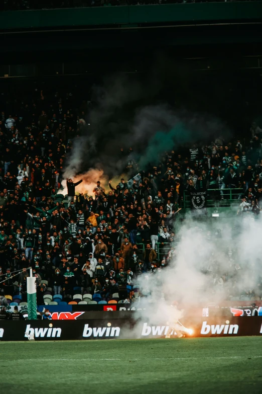 the smoke of a fan burns on a soccer field as a crowd watches