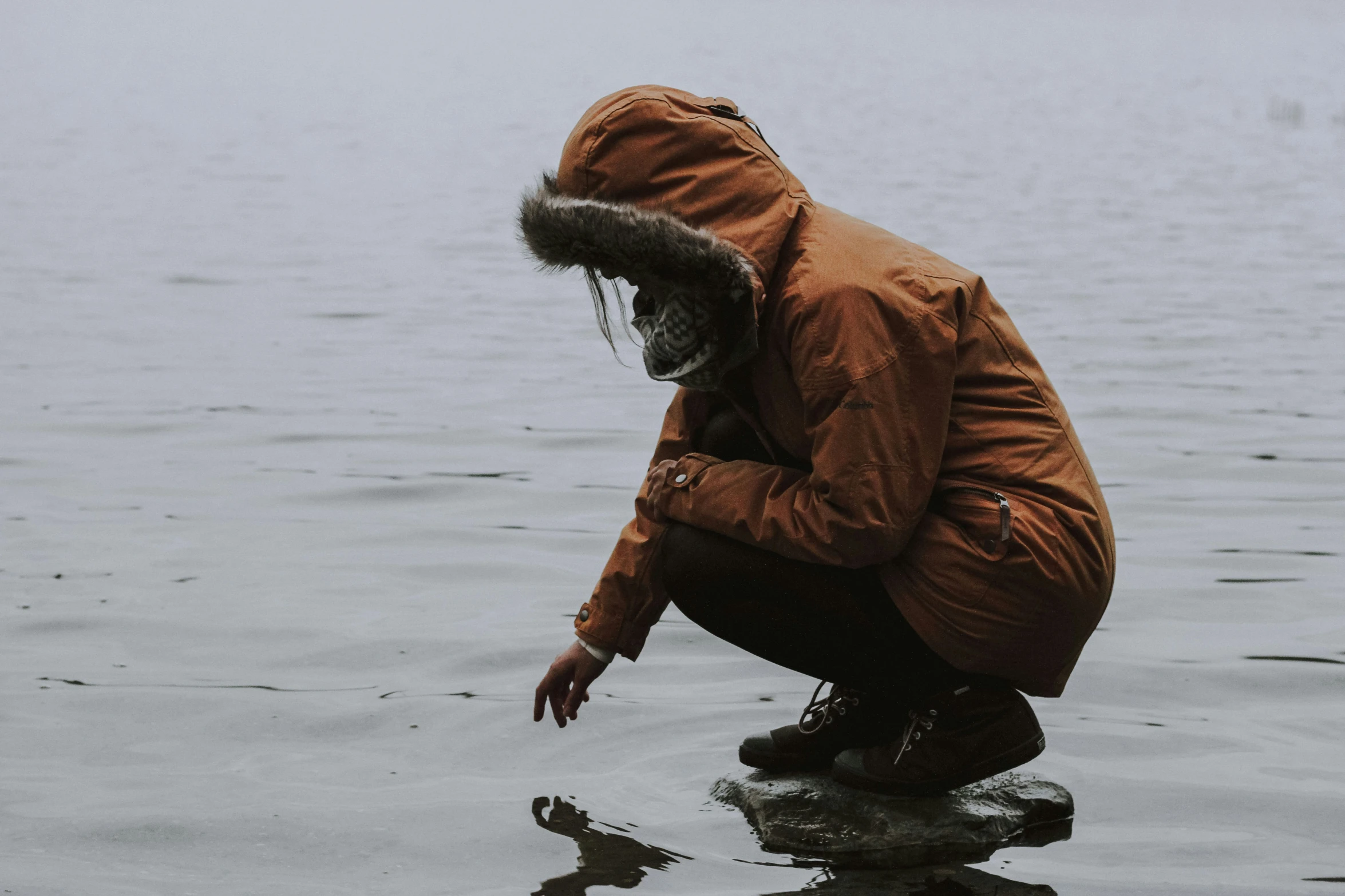 a man squatting in the water while standing on a rock