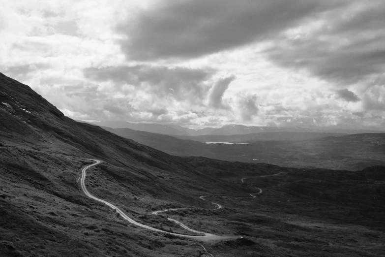 an aerial view of a hilly, winding road with storm clouds