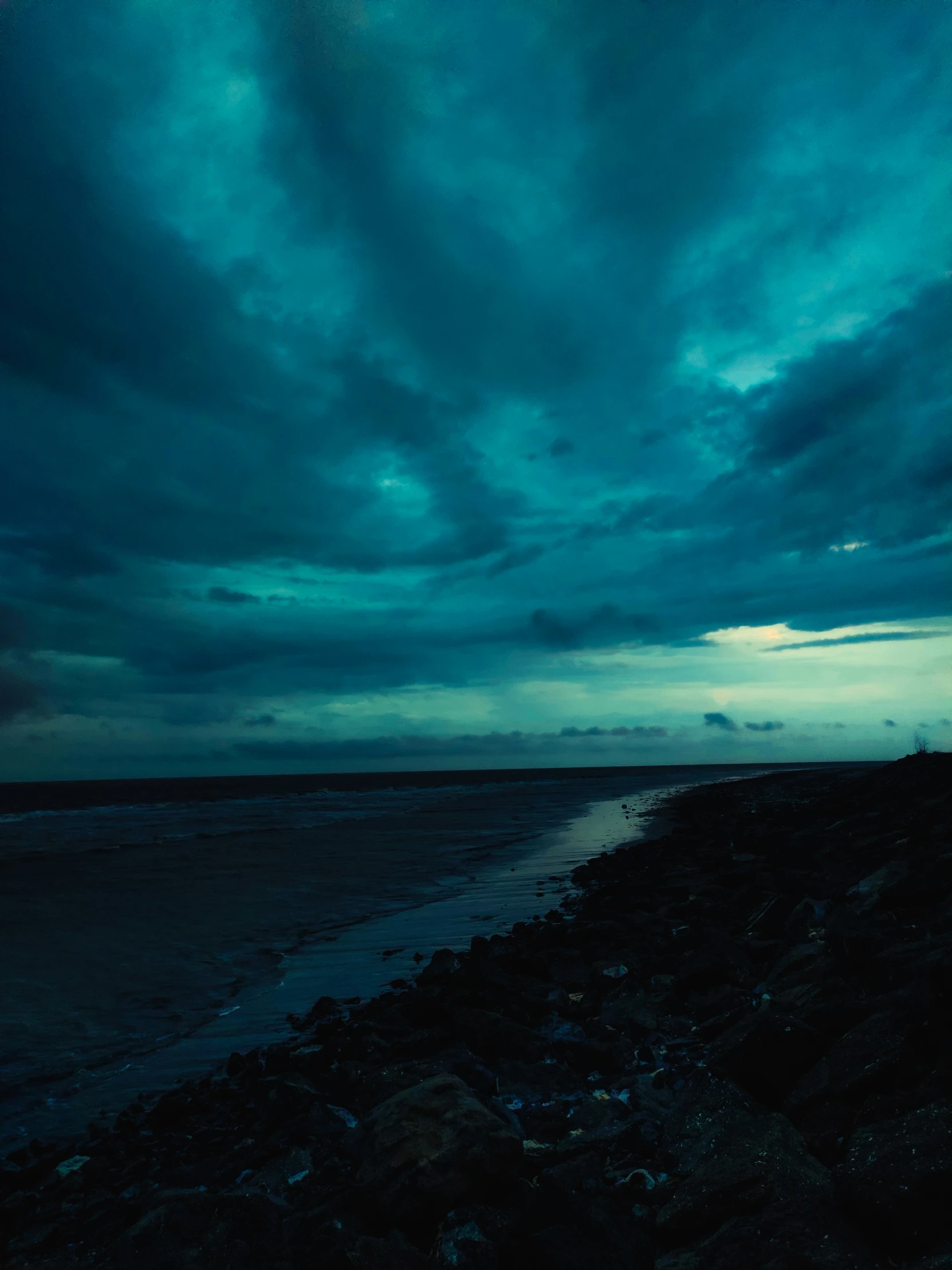 an empty road beside the ocean with a dark sky in the background