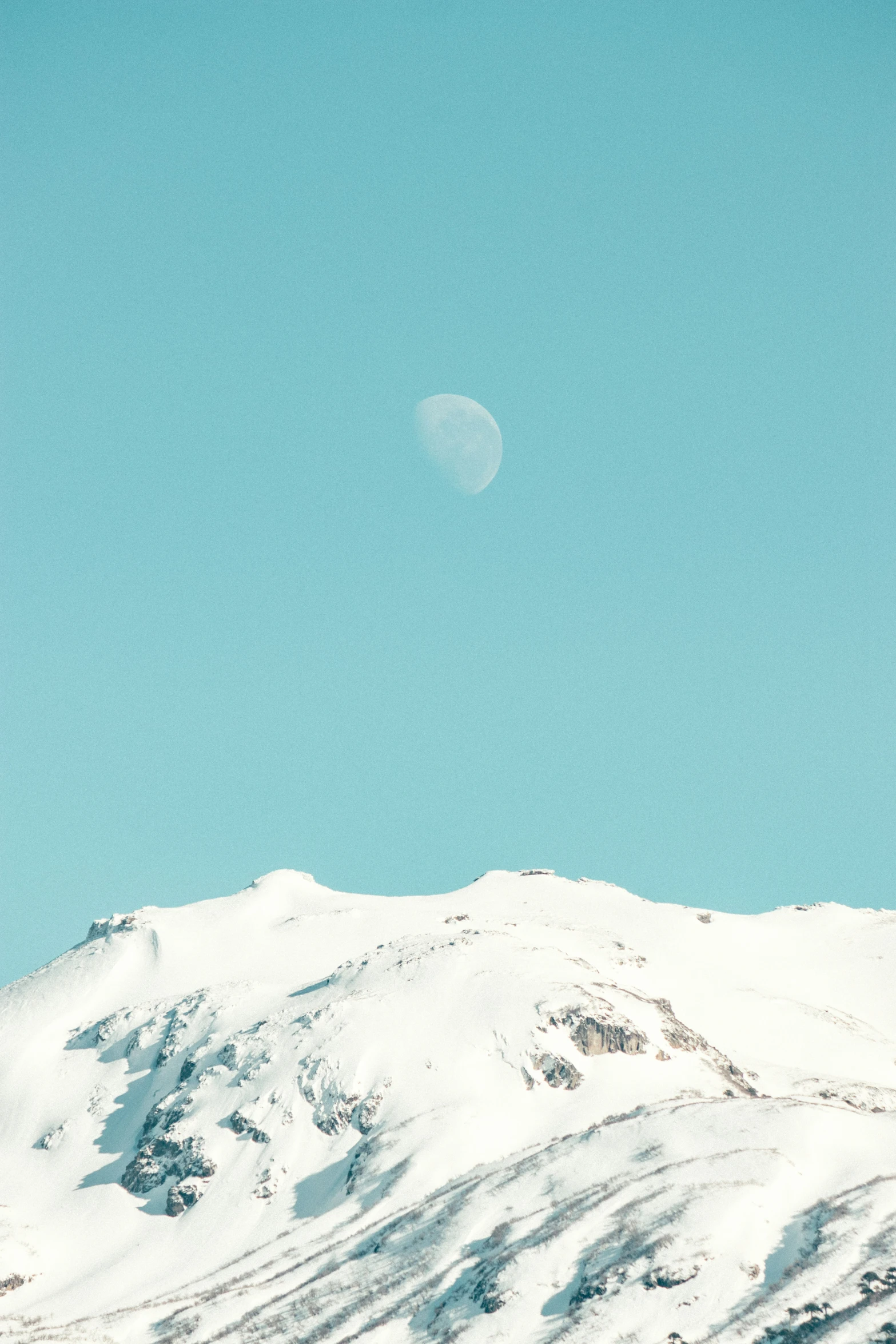 a full moon rising over some mountains under a blue sky