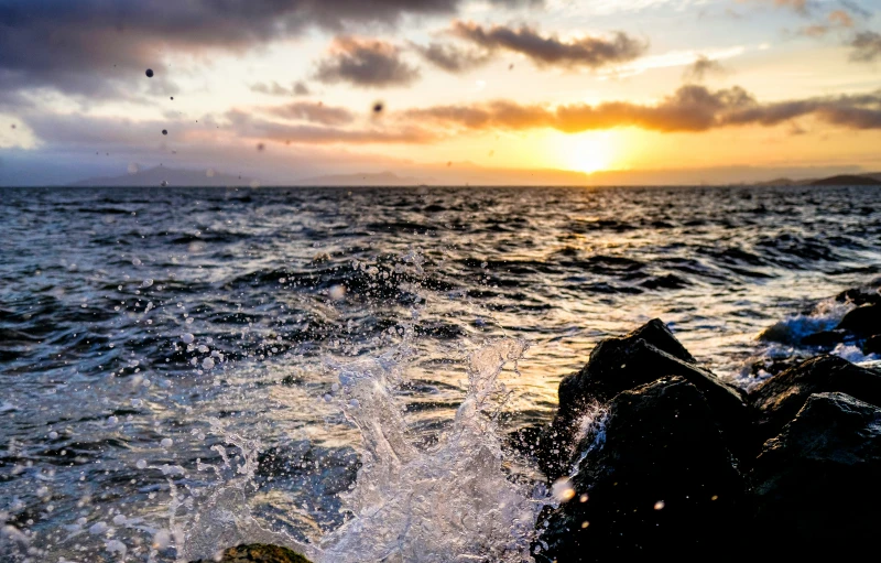 there is a rock in the water with the sun setting