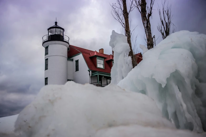 a lighthouse sits on top of ice at the top of a snowy hill