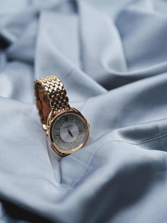 a gold wrist watch set on top of a white sheet