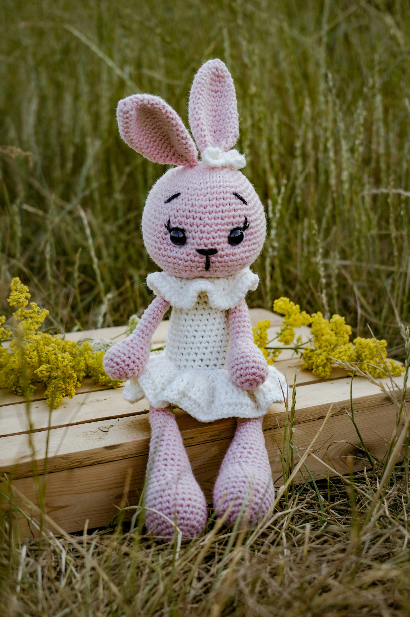 a crocheted stuffed rabbit sitting in tall grass