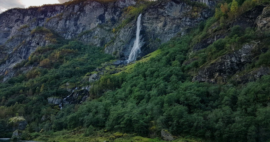 waterfall with mountains in background during cloudy day
