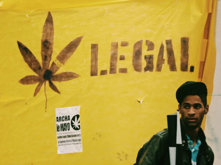 a young man standing next to a large yellow weed sign