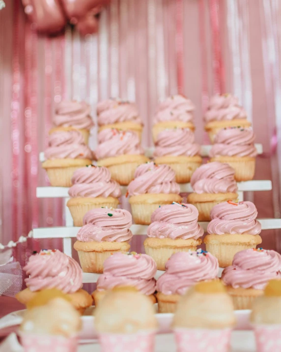 a bunch of cupcakes in pink icing on a table