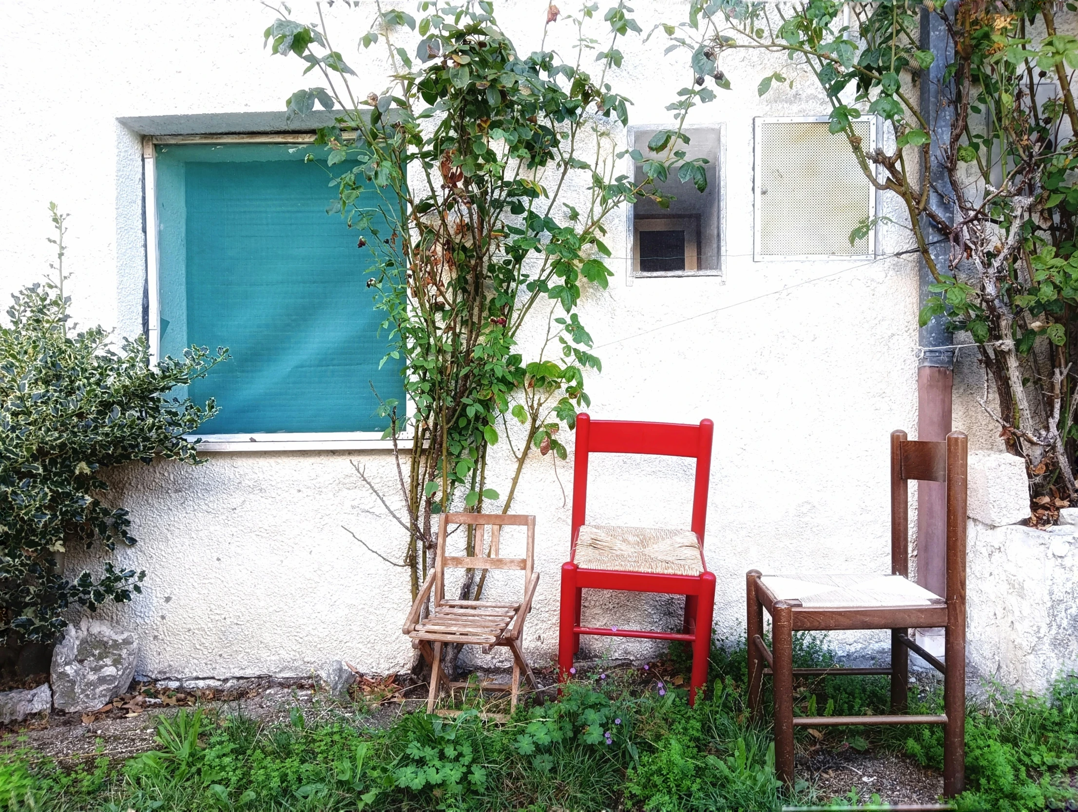 two red chairs and an old wooden chair against a white house