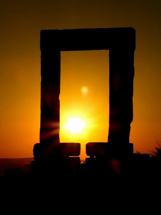 the sun is setting behind the silhouette of two large columns