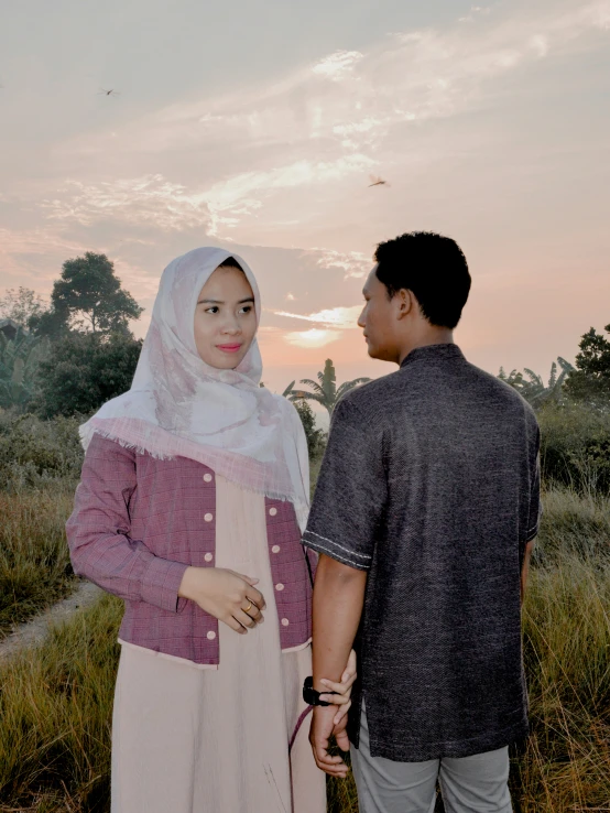 a man and woman standing in a grassy field with a kite flying in the sky