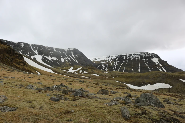 a large mountain with snow covered rocks and grass