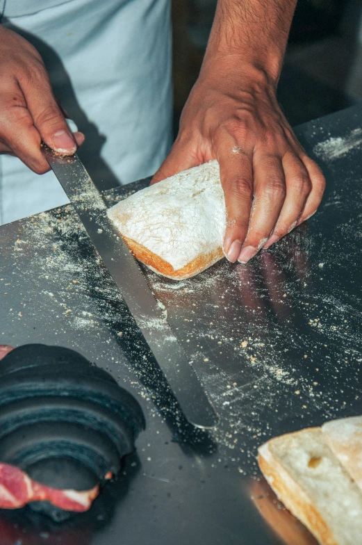 a chef using a long handled knife to cut a baguette on the table