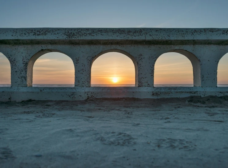 an archway sitting in the sand next to a body of water