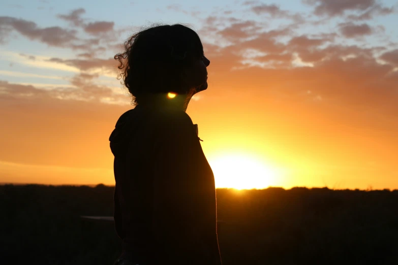 a silhouette image of a woman wearing headphones standing in front of the sun