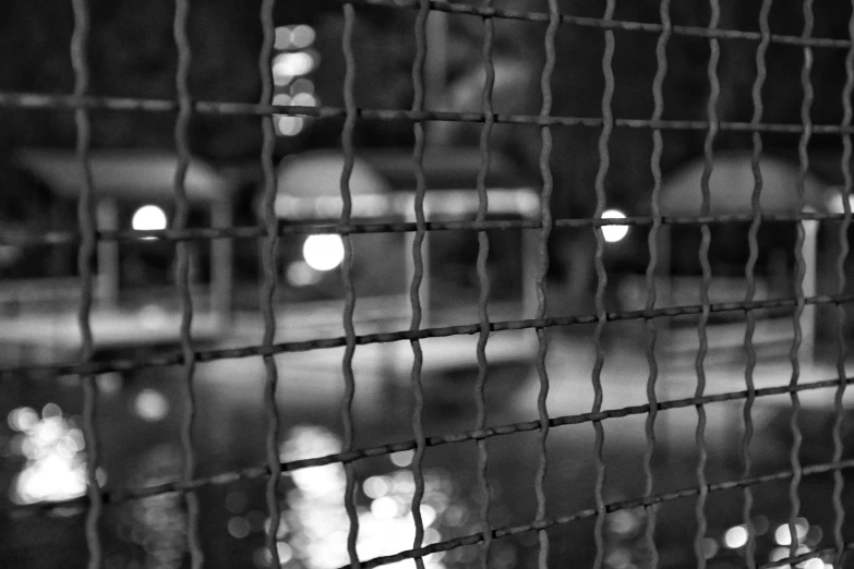 a view through a fence at night with lights