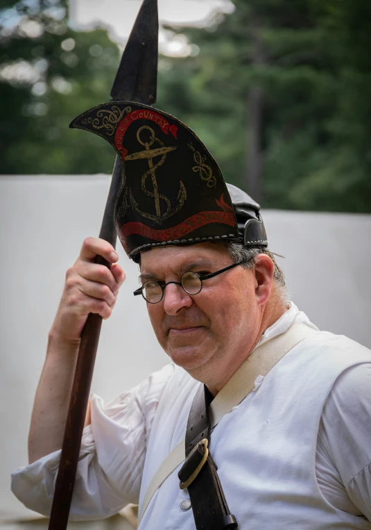 a man in glasses holding a large knife and wearing a hat