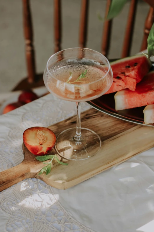 a glass of watermelon and pieces of apple sit on a wooden tray with a cloth dd over it