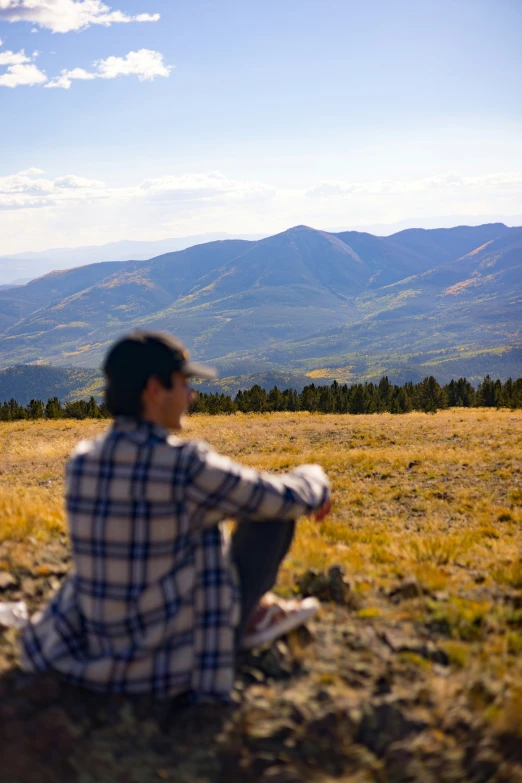 a man sitting in the grass looking at the mountains
