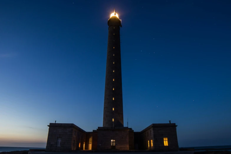 a lighthouse on the shore at night, lit up by bright light