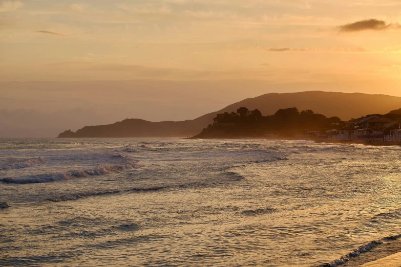 an ocean beach at sunrise with the sun setting behind two small island