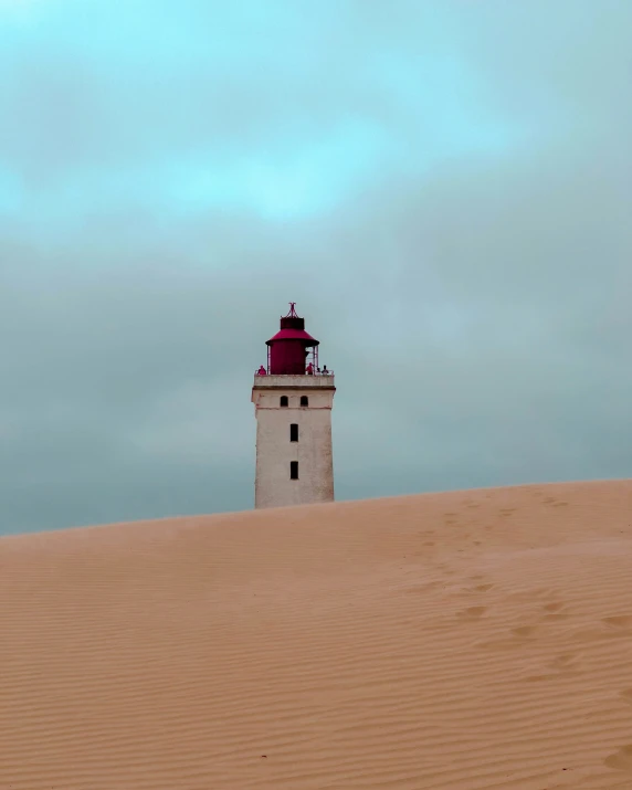 a red and white lighthouse on top of a large sand hill