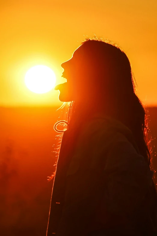 a woman standing in front of the sun at sunset