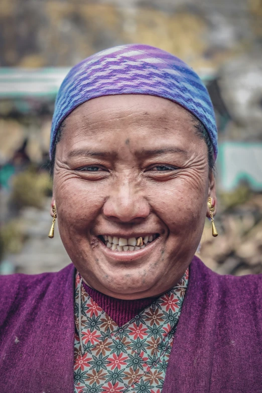 a smiling woman with a purple shawl, purple sweater and gold hoop earrings