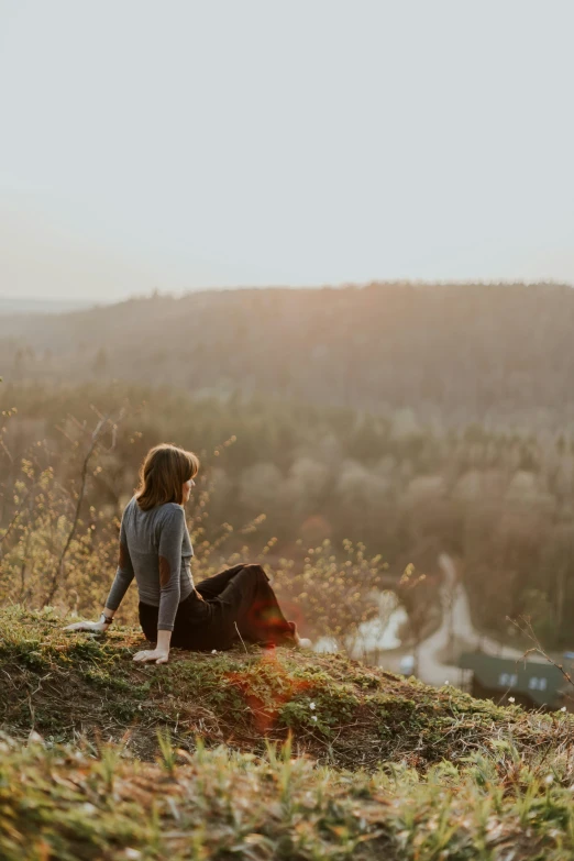 a woman is sitting on a hill looking at a dog
