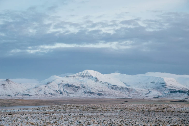 snow covered mountains loom in the distance behind rocky land