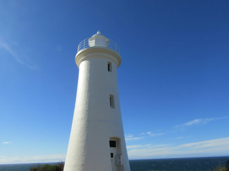 a white light house on the beach with a blue sky above