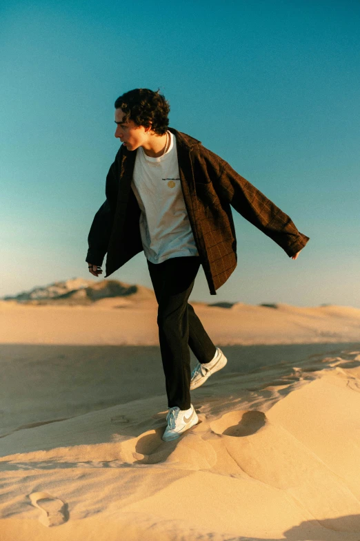 a boy in a white shirt and jacket is walking in sand