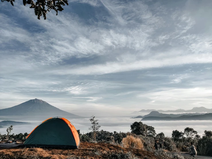 a tent is in the foreground near some trees and a mountain range