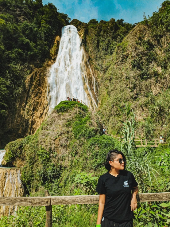 the woman stands beside a fence looking at the waterfall