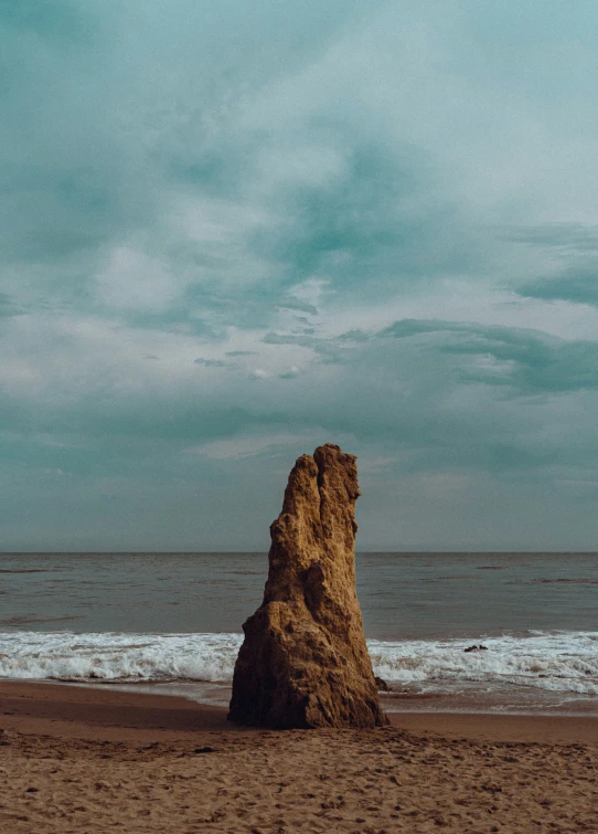 a rock sticking out of the sand next to the ocean